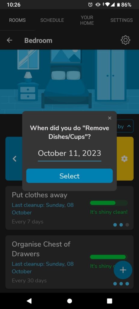 A screenshot of a phone. There is a square pop up with the heading When did you do "Remove Dishes/Cups?" Underneath is the date October 11th 2023. Behind it is a cartoon of a bedroom. Underneath are bubble with heading Put clothes away and Organise Chest of Drawers. They both have the date of last cleaning 08/10/2023 and full green sliding scale.